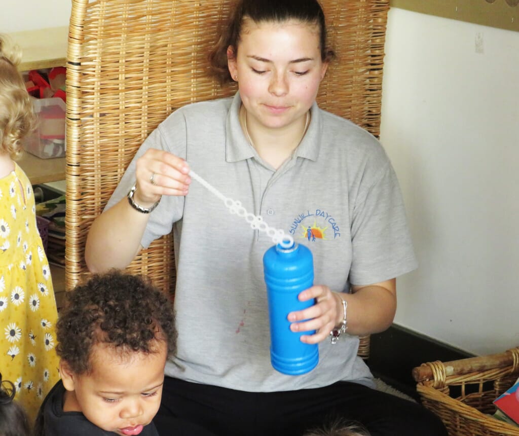 Nursery carer blowing bubbles for children