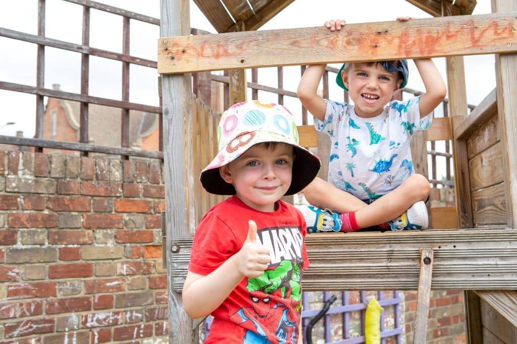 Two Pre-Schooler boys playing on outdoor apparatus, smiling and holding their thumbs up at the camera