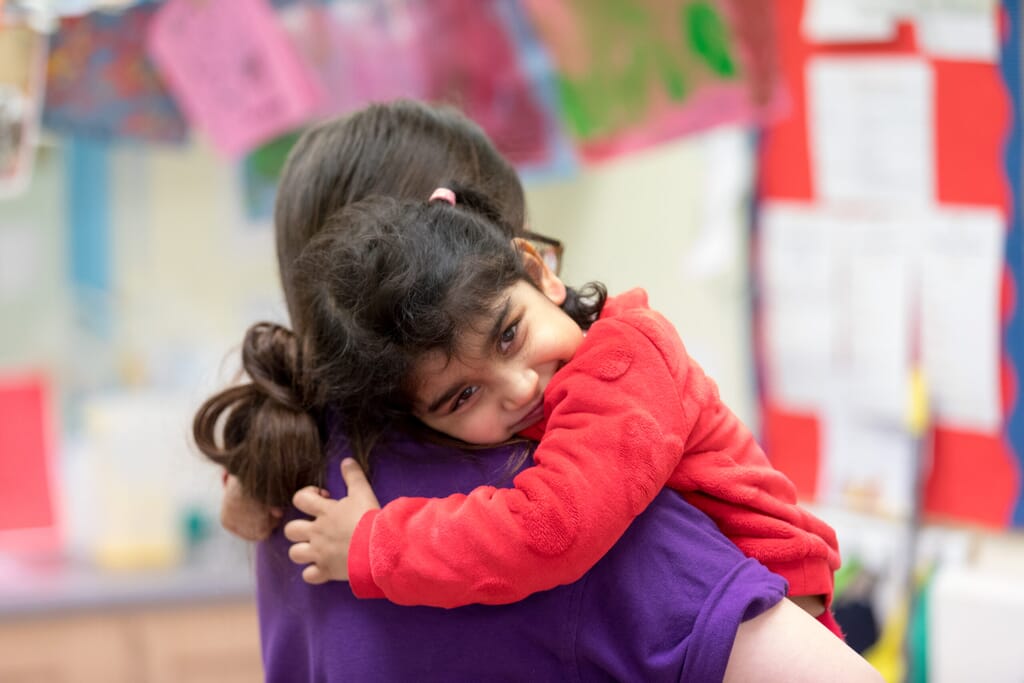 Nursery child hugging staff