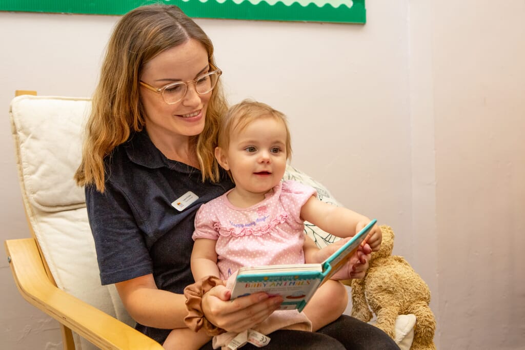 Nursery practitioner with a young girl on her lap reading her a book 