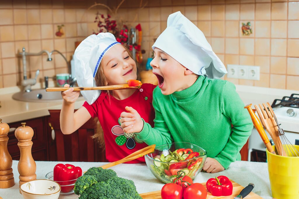 Two children trying to taste food in the kitchen