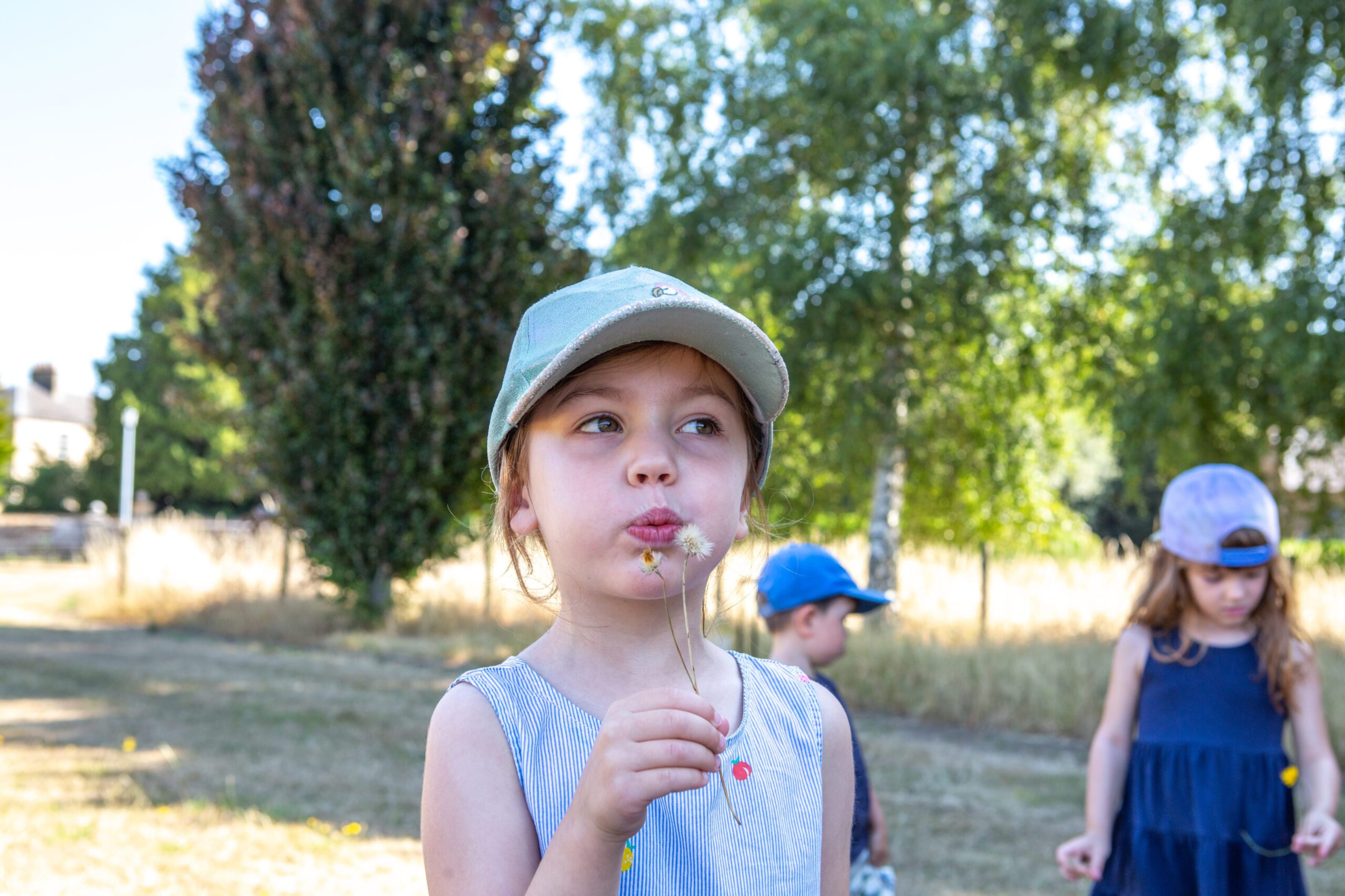 Girl blowing a dandelion outdoors in Forest School