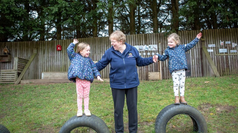 Nursery Practitioner supporting children on tyres in the outdoor area