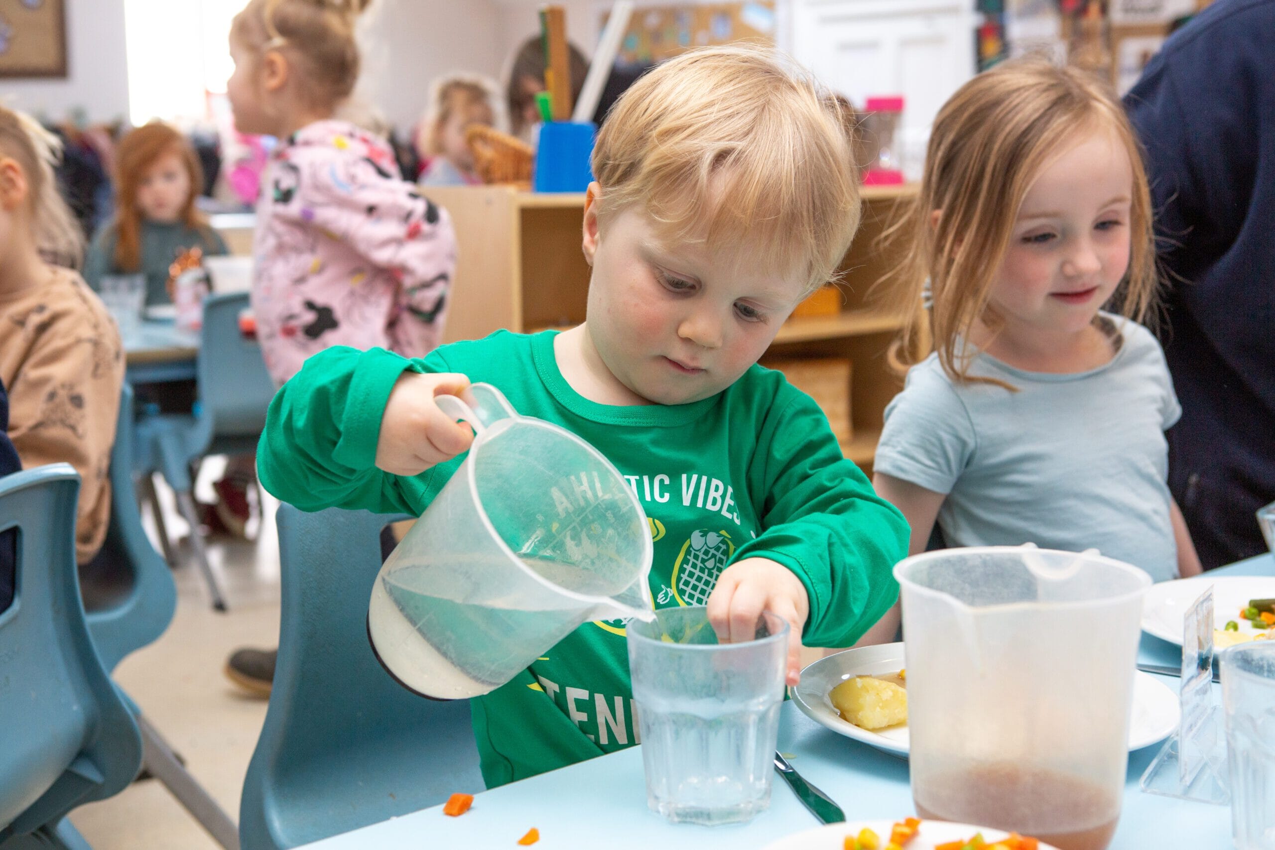 Child pouring a drink at nursery during mealtime